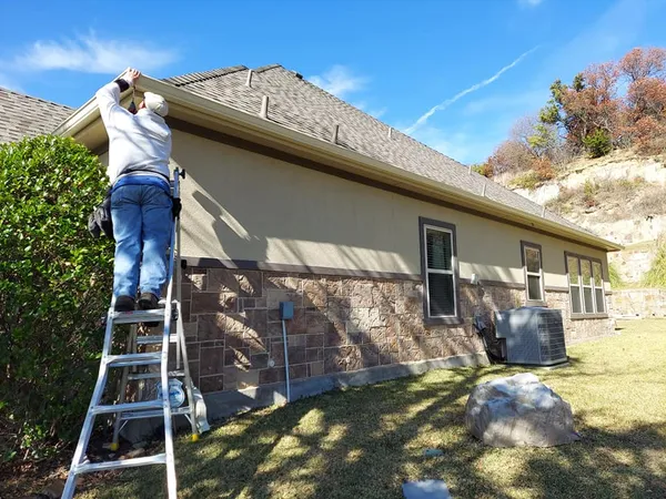 Beacon Rain Control technician installing seamless gutters on a stone home in Burleson, TX (February 2026)